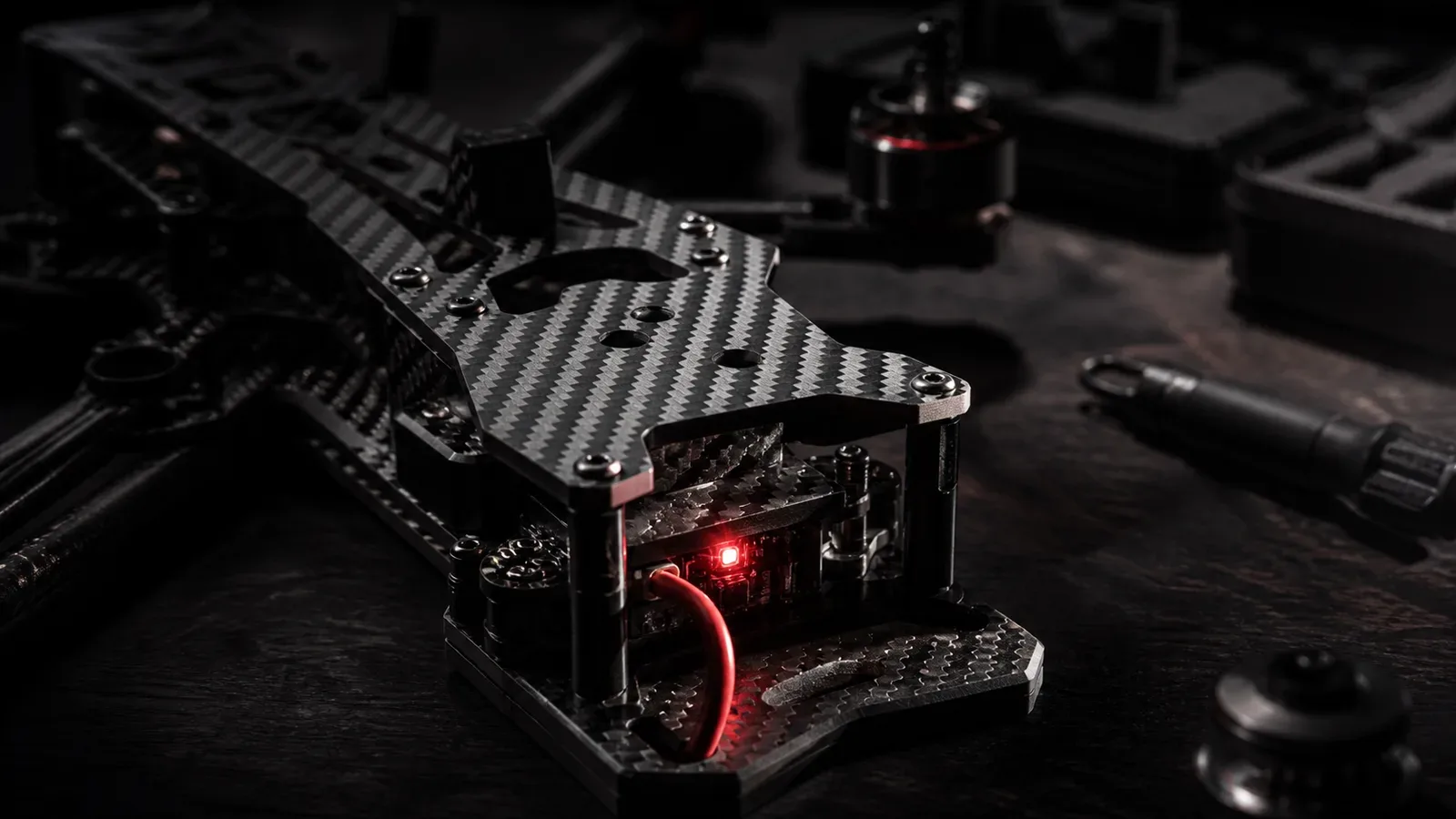 Close cinematográfico de placas de fibra de carbono usinadas em CNC montadas em chassi de Cinelifter FPV com indicador luminoso na bancada