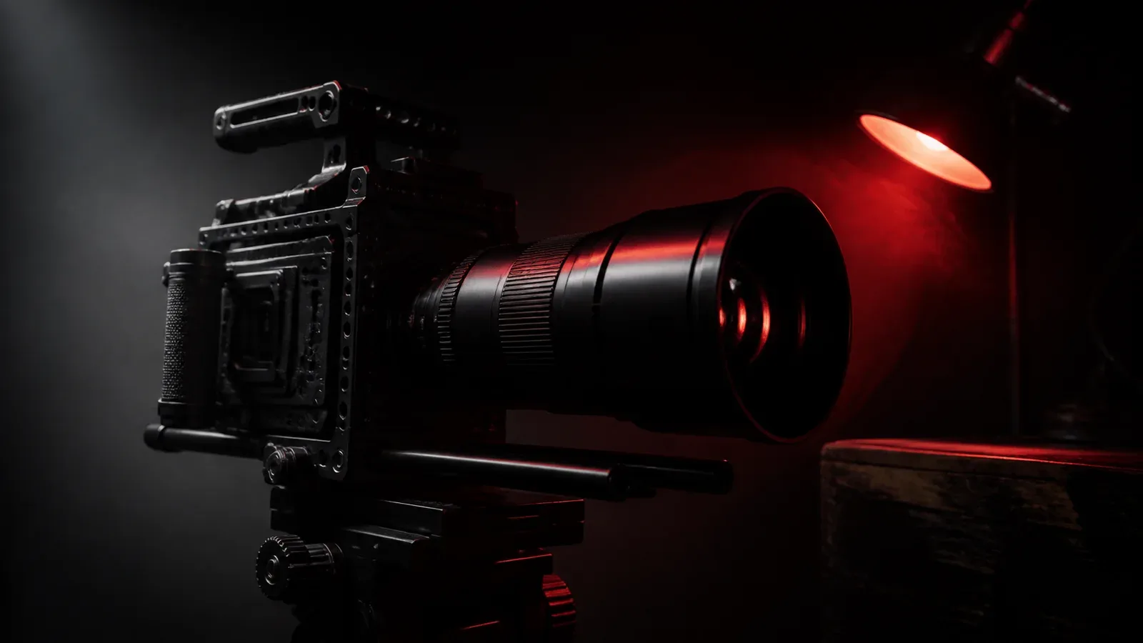 Câmera de cinema digital com lente anamórfica montada em cage em estúdio escuro com iluminação chiaroscuro e luminária acesa